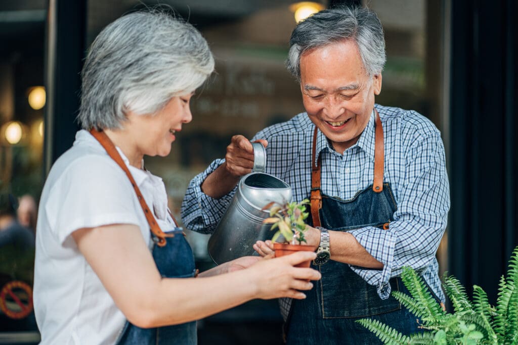 Man and woman, senior Taiwanese couple watering plants together.