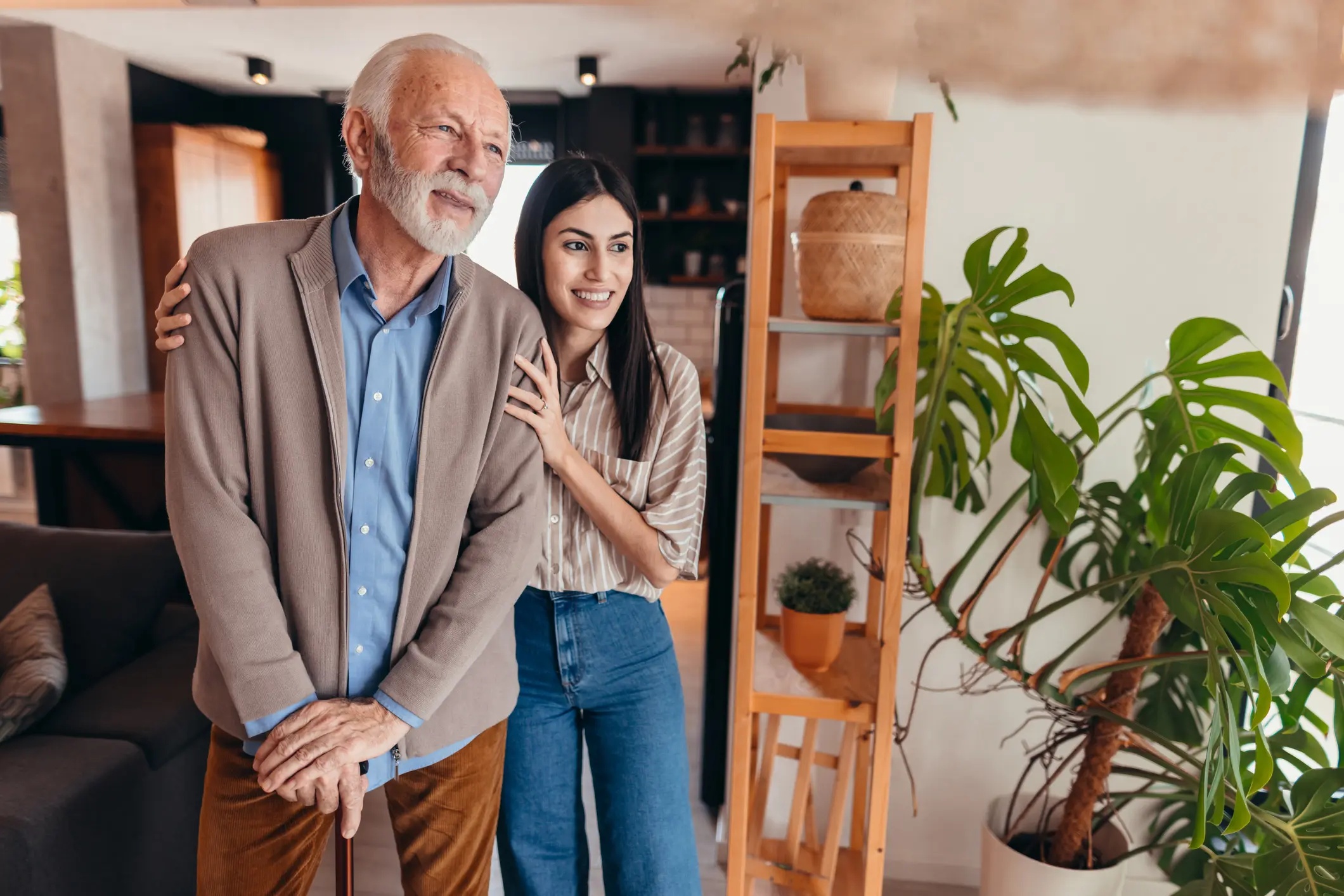 Young woman supporting senior man with a walking stick, fostering care and companionship in a warm, inviting home environment filled with comfort and connection